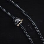 Close-up of a silver skull chain necklace with gold crossbones charm on a dark wooden background.